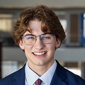 Smiling Financeable student with glasses in a navy suit and tie