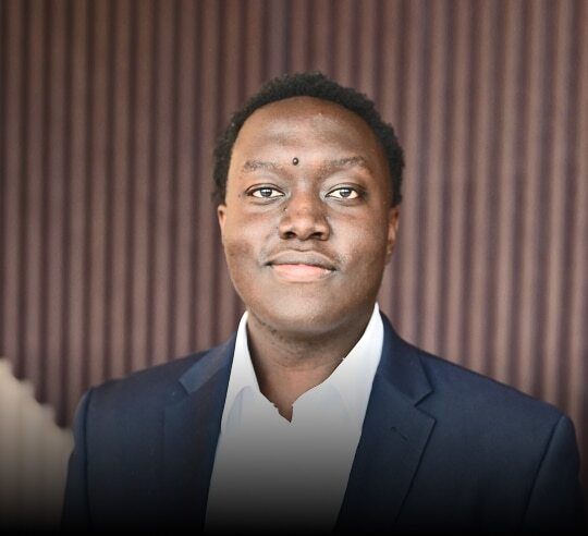 Smiling Financeable student in a navy suit against a striped wall