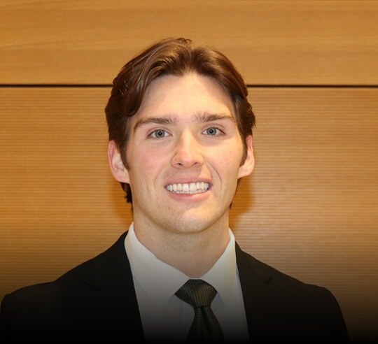 Smiling Financeable student in a dark suit and tie against a wood panel background